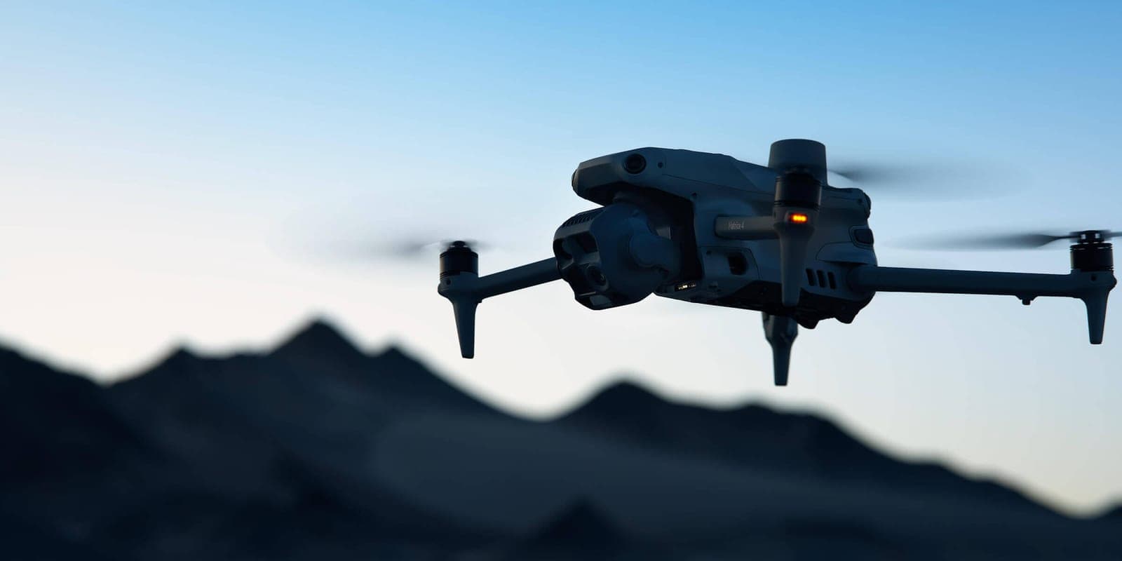 DJI Matrice 4 u letu iznad pustinjskog grebena, sklopivi krakovi rasklopljeni i propeleri u pokretu